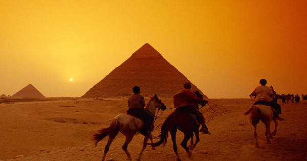 An image showcasing a group riding horses through the desert nearby the pyramids